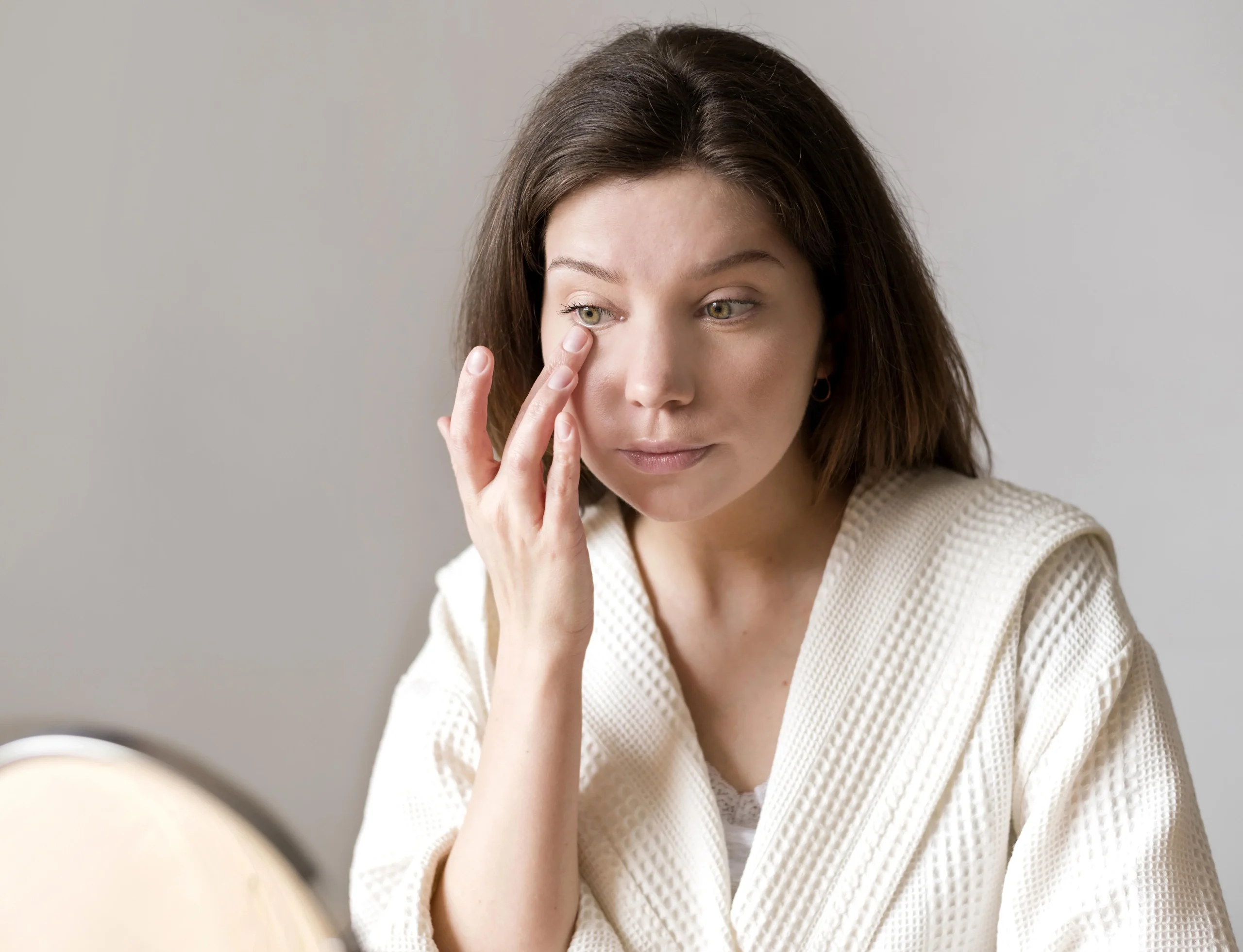 Mujer tocándose la zona de las ojeras frente al espejo